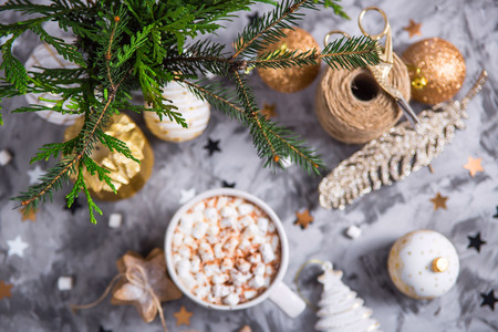 A large cup of cocoa with marshmallow sprinkled with cocoa powder stands on a gray table among Christmas decorations, fir branches, ginger cookies and shiny stars. Top viewの写真素材