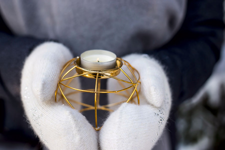 Golden metal candlestick in the hands of a woman in white mittens utdoor. Winter christmas moodの写真素材
