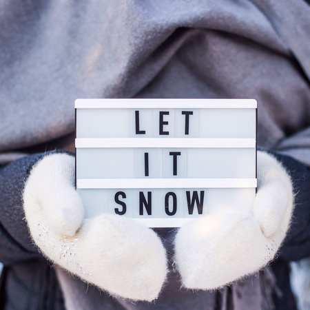 Let it snow it is written on a decorative lamp held by a woman in a gray scarf and white mittensの写真素材