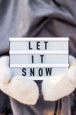 Let it snow it is written on a decorative lamp held by a woman in a gray scarf and white mittensの写真素材