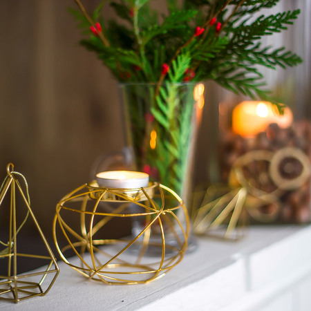 Home winter Christmas decorations in the apartment - candlesticks, a vase with green branches and red berries, golden figuresの写真素材