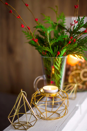 Home winter Christmas decorations in the apartment - candlesticks, a vase with green branches and red berries, golden figuresの写真素材
