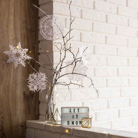Let it snow it is written on a decorative lamp next to a home winter decor with a vase with tree branches with paper snowflakes against a brick wall of an apartmentの写真素材