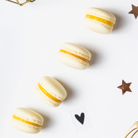 Yellow lemon macaroons on a white background next to golden Christmas decorations and asterisks. Festive tender French dessert. Top view, flat layの写真素材