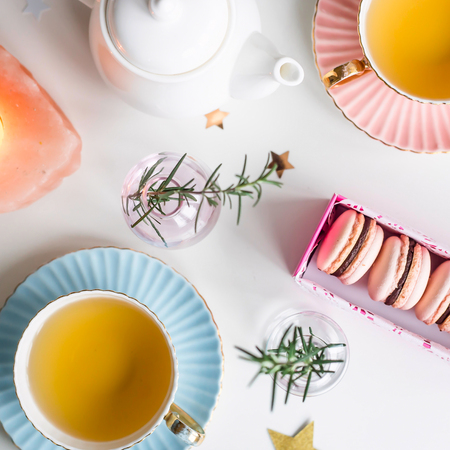 Gift box with pink macaroons among vintage cups of green tea, stars and small vases with sprigs on a white background. Stylish dessertの写真素材