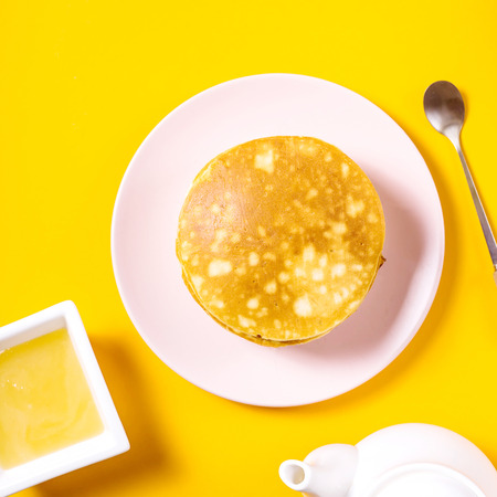 A stack of pancakes on a pink plate next to a plate of honey on a bright yellow background. Top viewの写真素材