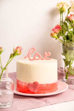 White cake with pink decor and the word love on top among small white and pink roses. Valentine's Day Gift Conceptの写真素材