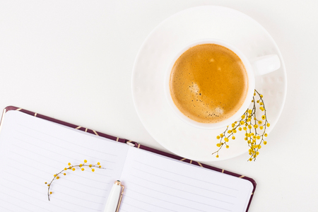 Springtime workplace with a cup of coffee and a mimosa flower next to an open notepad. Top view, flat layの写真素材