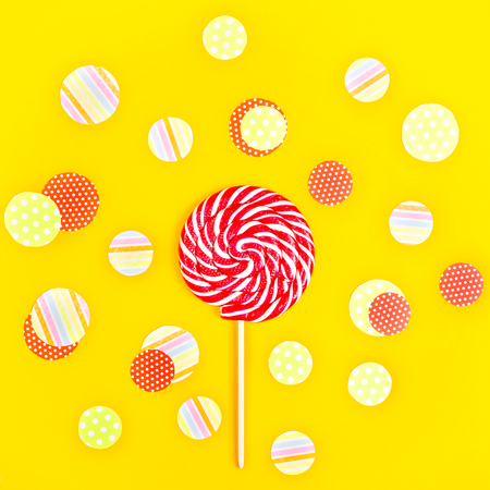 Multicolored spiral candy on a bright yellow background in the middle of multicolored confetti circles. Top view, flat layの写真素材