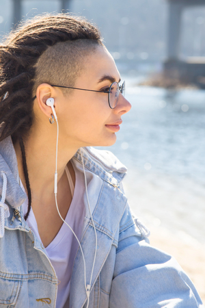 Stylish caucasian girl listening to music with headphones and resting in nature in springの写真素材
