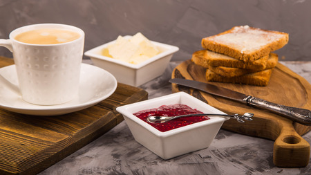 Breakfast of toast with butter and raspberry jam next to a cup of coffeeの写真素材