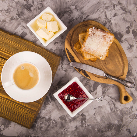 Breakfast of toast with butter and raspberry jam next to a cup of coffee. Top view, flat layの写真素材