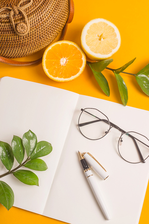 Bright yellow summer desktop with fruit and a white open notebook next to glasses and a pen. Top view, flat layの写真素材