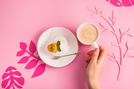 Pavlova dessert from meringue with mango rosette on a white saucer among pink paper tropical leaves on a bright background. Top view, flat layの写真素材