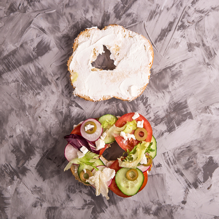 Bagel with sesame cooked sandwich with vegetables and cheese on a gray concrete background. Top view, flat layの写真素材