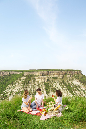 Three young beautiful girls relaxing on a picnic in nature and drinking wine in the mountainsの写真素材