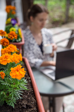 A girl works at a laptop sitting with a cup of cappuccino at an outdoor cafe table. concept of modern life and freelancingの写真素材