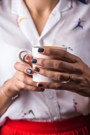 A girl with a beautiful modern manicure with shabby gold is holding a white cup of cappuccinoの写真素材