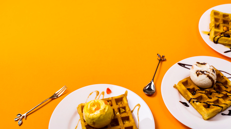 Fresh golden square Belgian waffles on plates with ice cream and toppings on a bright yellow background. Copy spaceの写真素材