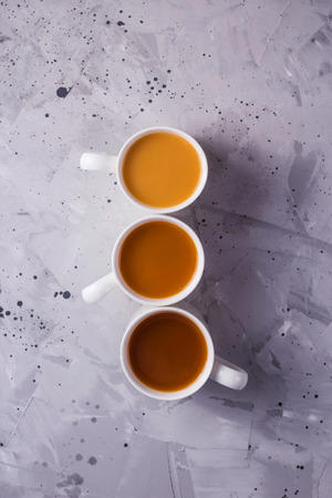 Three cups of masala tea or coffee with milk of different colors on a gray textural background. Top view, flat layの写真素材