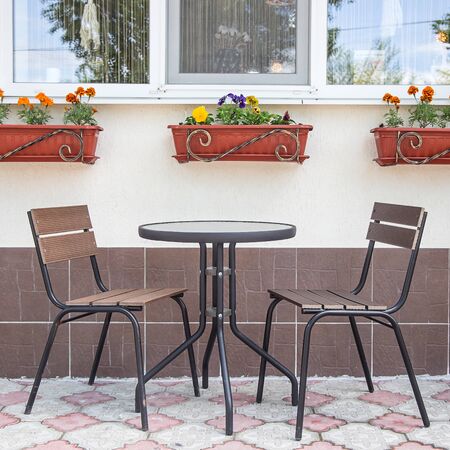 Glass and metal tables and chairs on a summer terrace cafe by the window with pots of flowersの写真素材