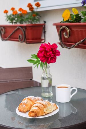 Two croissants on a plate next to a cup of cappuccino on a street table of a summer terrace cafe. Beautiful breakfast outdoorの写真素材