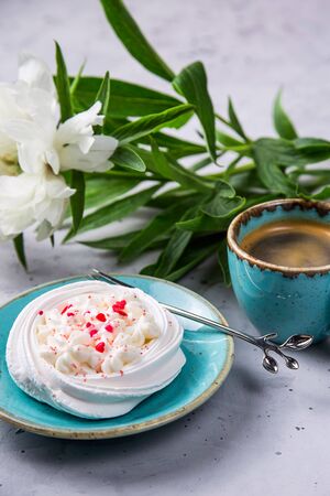 Dessert pavlova meringue with whipped cream and pink decoration next to a cup of coffee and white peonyの写真素材