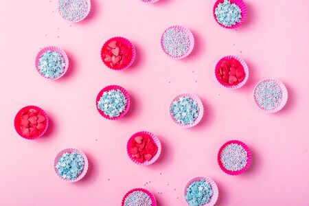 Small pink silicone molds for baking muffins or making sweets filled with colorful sugar decorations for desserts on a pink background. Top view, flat layの写真素材