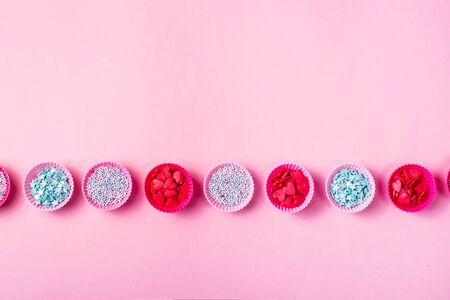 Small pink silicone molds for baking muffins or making sweets filled with colorful sugar decorations for desserts on a pink background. Top view, flat lay, copy spaceの写真素材