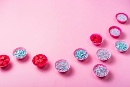 Small pink silicone molds for baking muffins or making sweets filled with colorful sugar decorations for desserts on a pink background. Top view, flat lay, copy spaceの写真素材