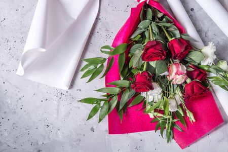 Beautiful bouquet with red roses and green leaves on red and white paper - the process of creating a bouquetの写真素材