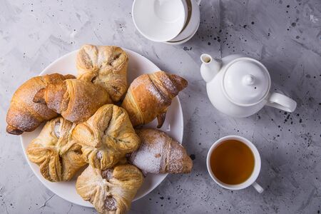 Sweet puff pastry fresh and covered with powdered sugar on a gray table next to the kettle and cups for teaの写真素材
