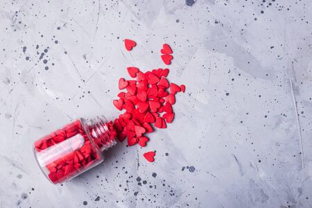 Transparent bottle with red sugar hearts to decorate baking and cakes on a gray table. Valentine's day concept. Top view, flat lay,の写真素材