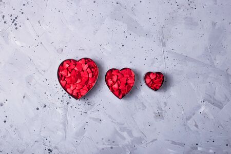 Three metal heart shape cookies for cookies full of red sugar hearts on a gray table. Valentine's day concept. Top view, flat layの写真素材