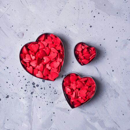 Three metal heart shape cookies for cookies full of red sugar hearts on a gray table. Valentine's day concept. Top view, flat layの写真素材