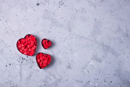 Three metal heart shape cookies for cookies full of red sugar hearts on a gray table. Valentine's day concept. Top view, flat lay, copy spaceの写真素材