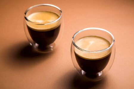 Black American coffee in a transparent glass with double glass on a neutral brown backgroundの写真素材