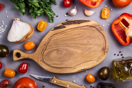 Empty wooden cutting board with place for text among the ingredients for cooking vegetable dish with tomatoes, pepper, garlic. Top view, flat lay, copy spaceの写真素材