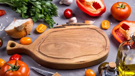 Empty wooden cutting board with place for text among the ingredients for cooking vegetable dish with tomatoes, pepper, garlic. Copy spaceの写真素材