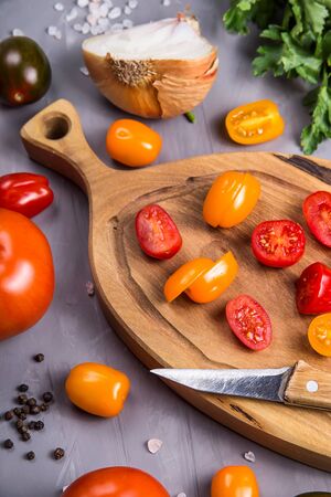 Cherry tomatoes sliced on a wooden board among other vegetables for cooking on a gray background. Top view, flat layの写真素材