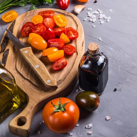 Cherry tomatoes sliced on a wooden board among other vegetables for cooking on a gray backgroundの写真素材