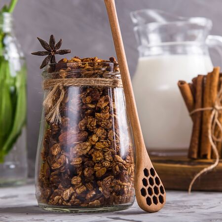 Dry homemade chocolate granola in a jar next to a jug of milk on a gray tableの写真素材
