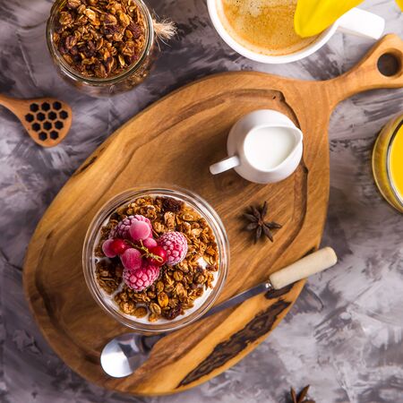 Dessert with granola and yogurt berries in glasses with double glass for breakfast next to coffee, flower and juice. Top view, flat layの写真素材