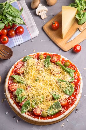 Round homemade vegetarian pizza with cheese, mushrooms, cherry tomatoes and basil among the ingredients for cooking. Top view, flat layの写真素材