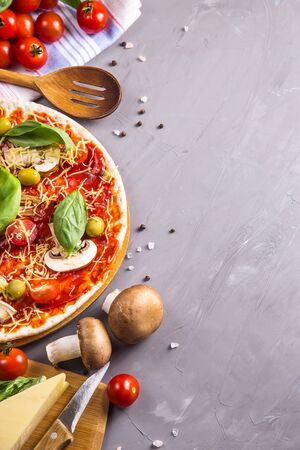 Round homemade vegetarian pizza among the ingredients for cooking on a gray table. Top view, flat lay, copy spaceの写真素材