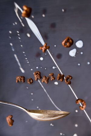 The word morning is written with chocolate cornflakes for a quick breakfast with milk on a gray background with levitationの写真素材