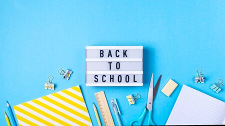 Bright modern minimalist stationery for school on a blue background next to a decorative lamp with the inscription back to schoolの写真素材