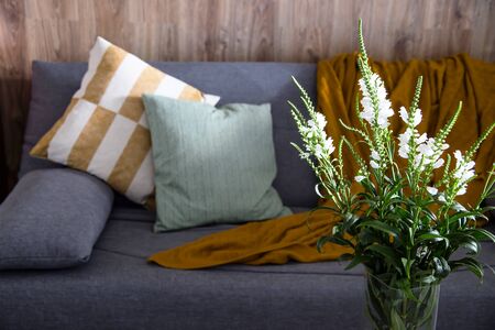 A bouquet of white spring flowers in the interior near the gray sofa with green and yellow pillows. Home comfort in the interiorの写真素材