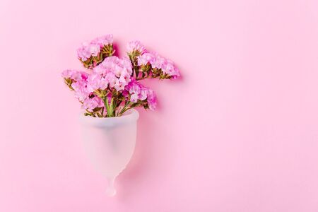 White menstrual cup for women next to flowers on a pink background. Ecological alternative to gaskets and tampons. Zero waste conceptの写真素材