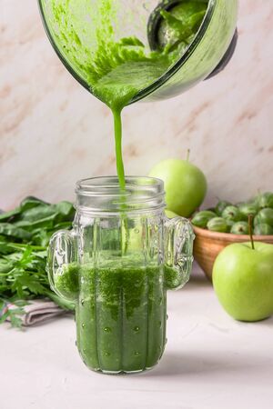 Green smoothies are poured from a glass blender bowl into a glass in the shape of a cactus. Healthy raw food and detox conceptの写真素材